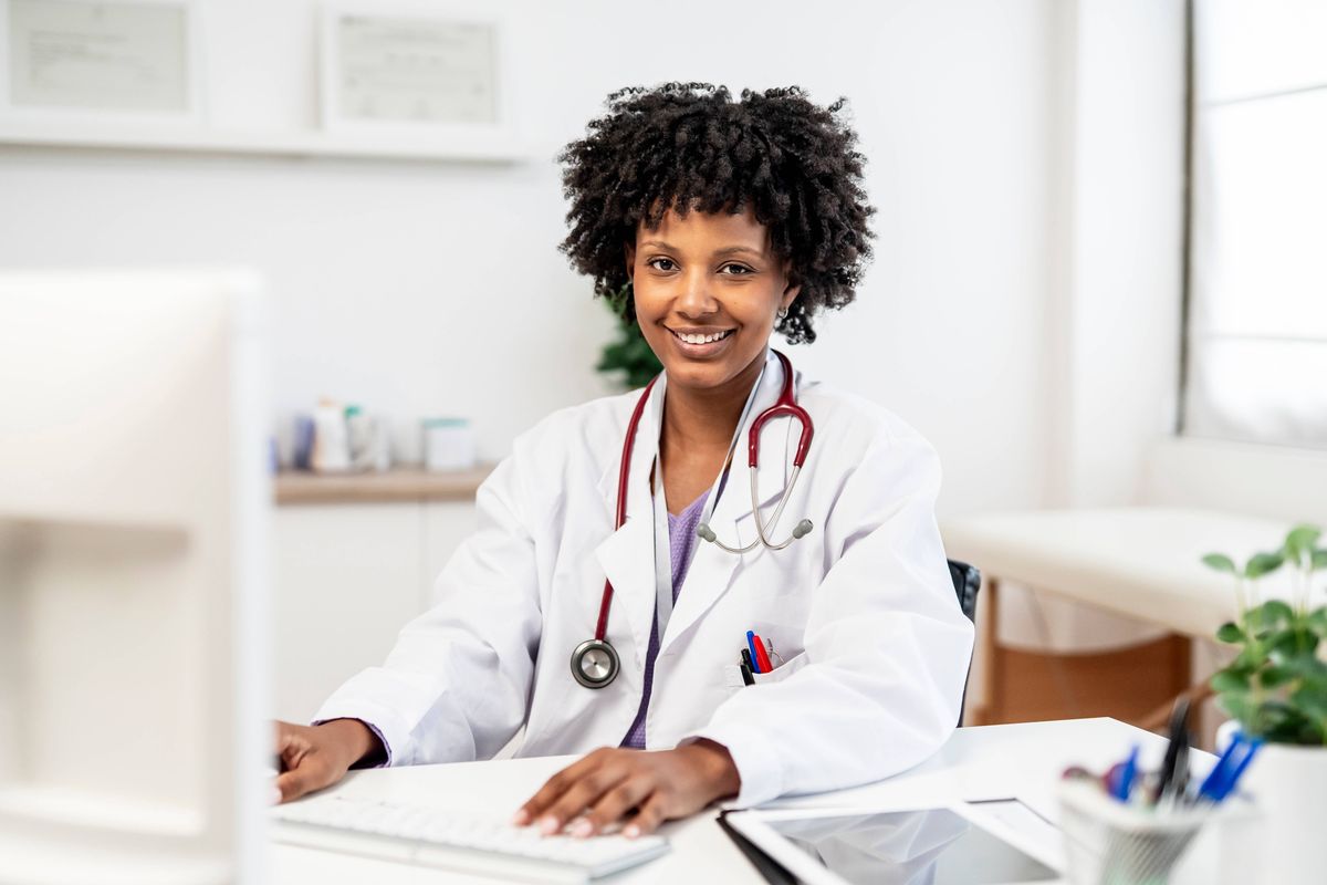 Confident female doctor smiling at the camera while using a computer in a modern clinic, showcasing professionalism and expertise