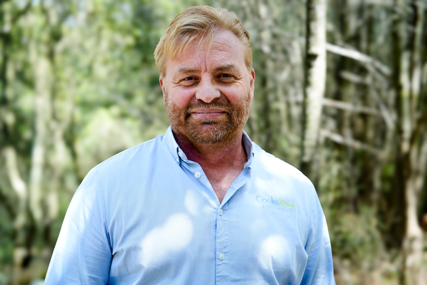 Dr Thomas smiling at the camera standing in front of trees.
