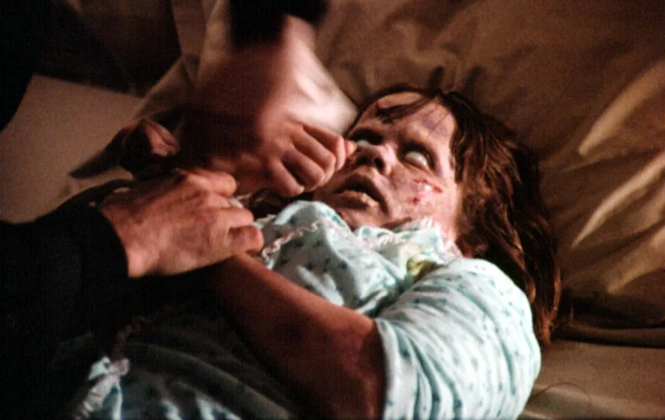 A person lies in bed with a distressed facial expression, appearing to be involved in a dramatic or horror scene