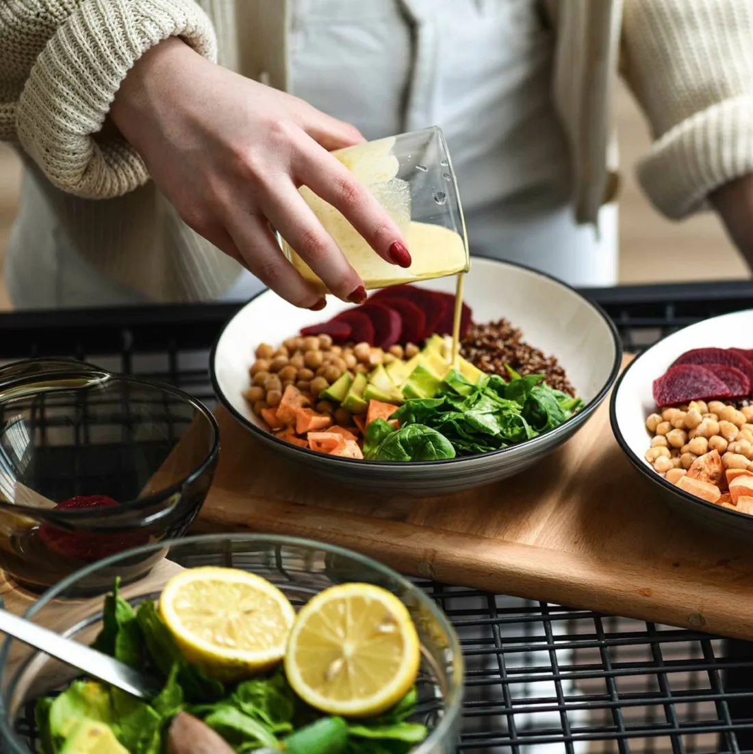 Photo of a person pouring a dressing onto a healthy salad with greens, beans and other healthy foods