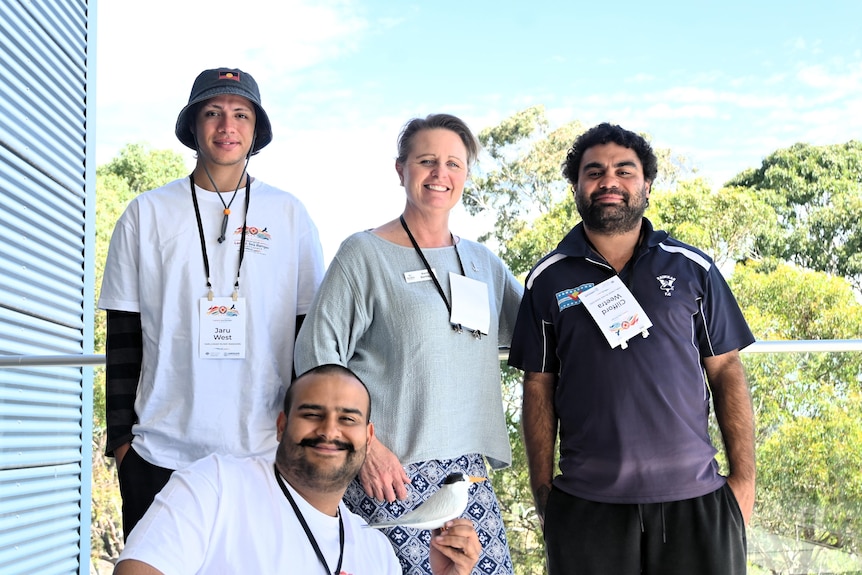 Three men, one holding a model of a fairy tern with a woman on a verandah