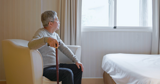 An Asian man is looking out the window from his house [GETTY IMAGE PRO]