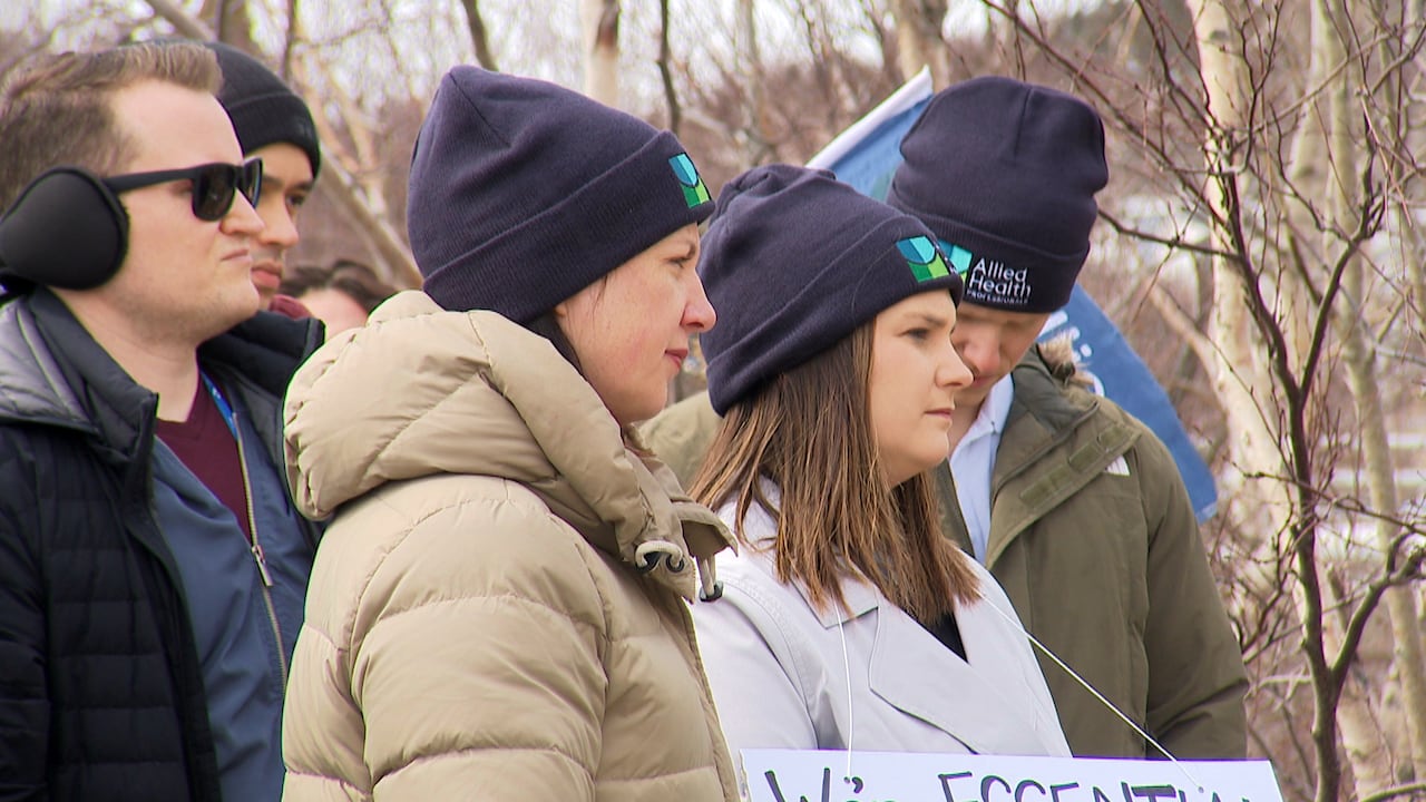 Two women wearing winter coats stand next to each other at a rally.