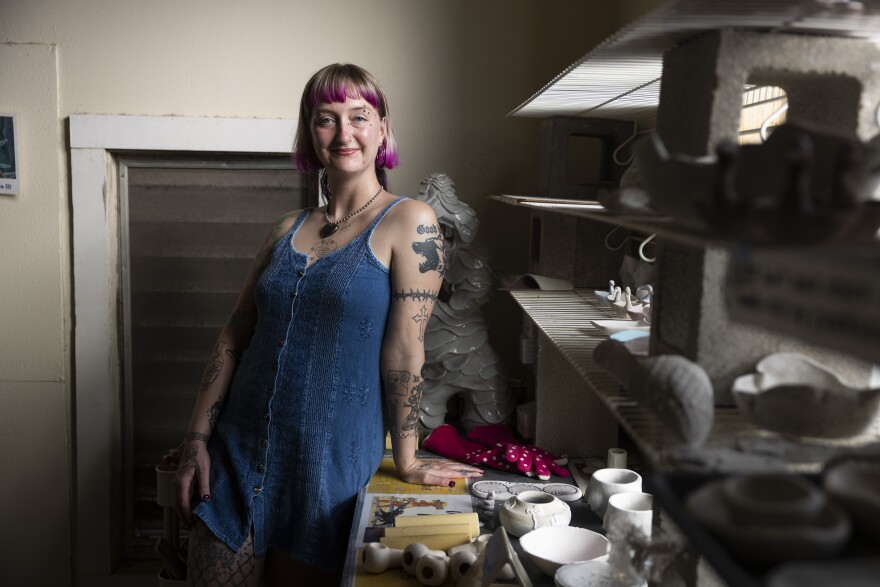 A woman leans against a table inside a pottery studio as she poses for a photo