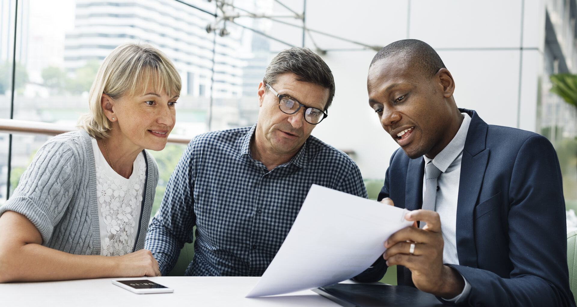 A man and a woman look at a paper that another man is showing them.