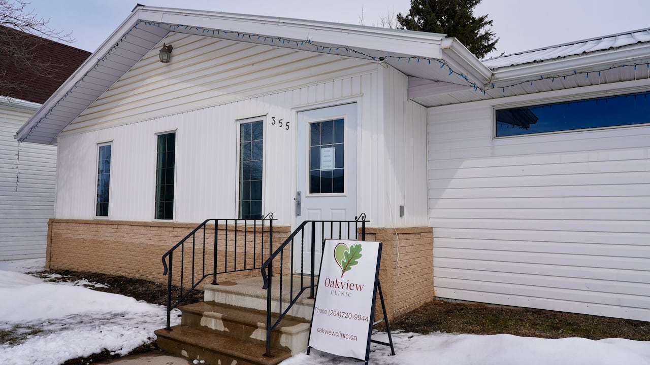A layer of snow is on the lawn of a white building that has three steps, with a sign on a stand that says Oakview Clinic.