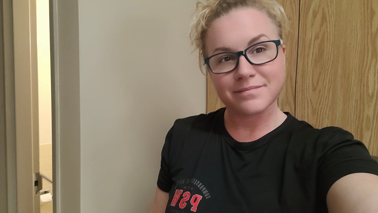 Woman with blonde hair and glasses takes selfie wearing a black T-shirt with red PSW logo on it
