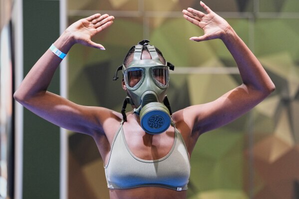A woman exercises while she wears a military NBC protective mask at a German Army promotion stand during the health & fitness trade show FIBO in Cologne, Germany, Friday, April 17, 2026. (AP Photo/Martin Meissner)