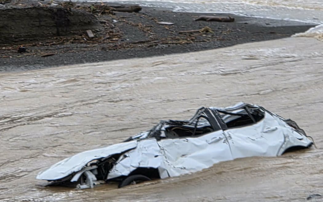 A car is submerged in the river mouth where the stream flows onto the beach in Ōwhiro Bay