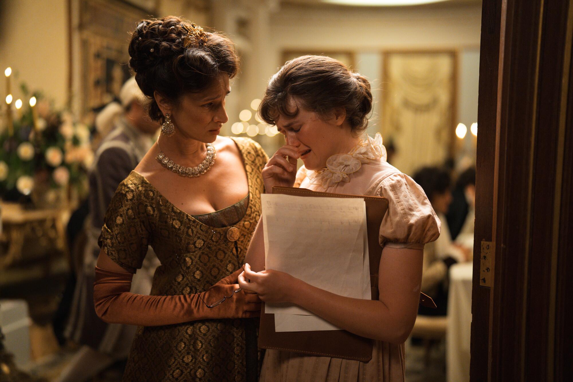 An older woman comforts a younger woman who is crying and holding sheets of music.