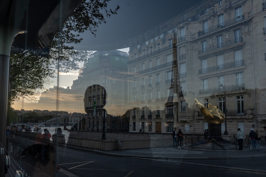 A man's silhouette reflected in a glass window in Paris. The Eiffel Tower is reflected in the window next to him.