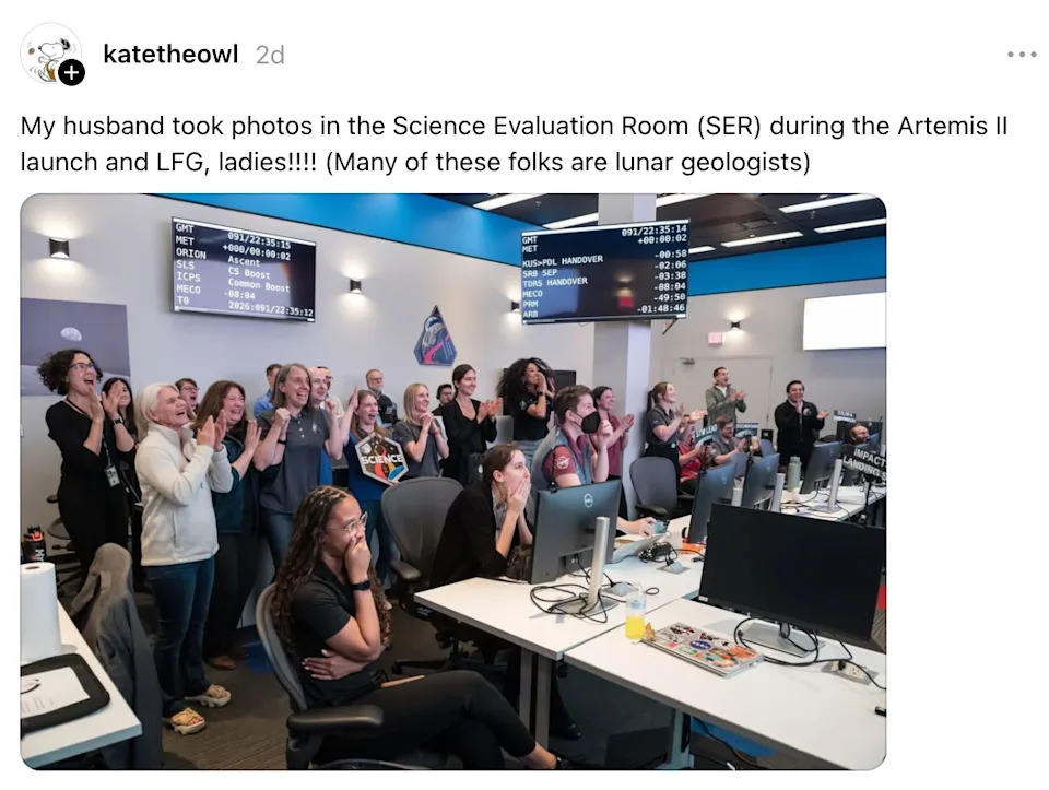 Group of people in a control room celebrating the launch of Artemis II, with screens showing mission details