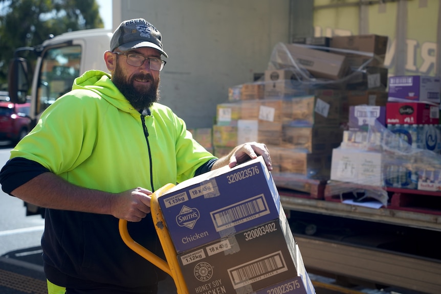 A man in a high-vis jumper unloads boxes of food from the back of a truck.
