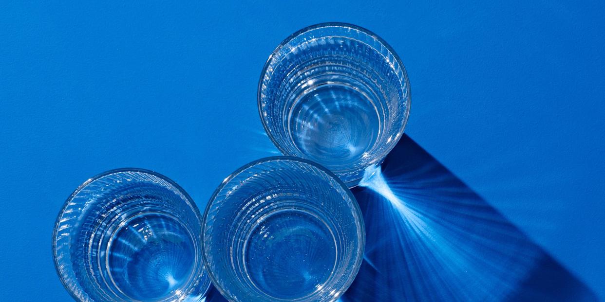 glasses of clear protein drinks with long shadow on deep blue colored background view