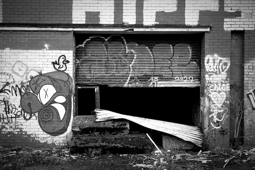Half-opened roller door at an abandoned building with graffiti on the brick walls.