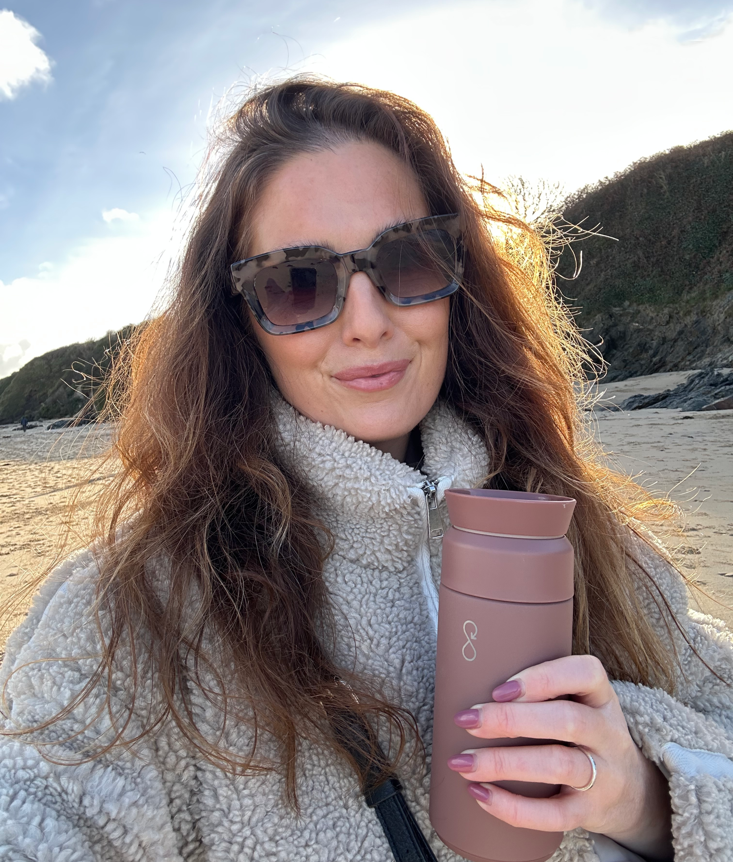 Georgie Shannon posing with sunglasses and a reusable bottle on a beach.