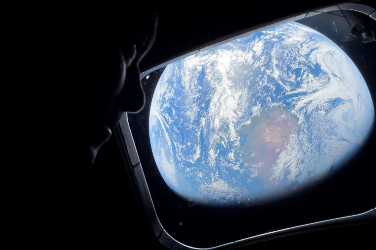 Image: Close up of an astronaut looking out of a spacecraft window with a view of Earth