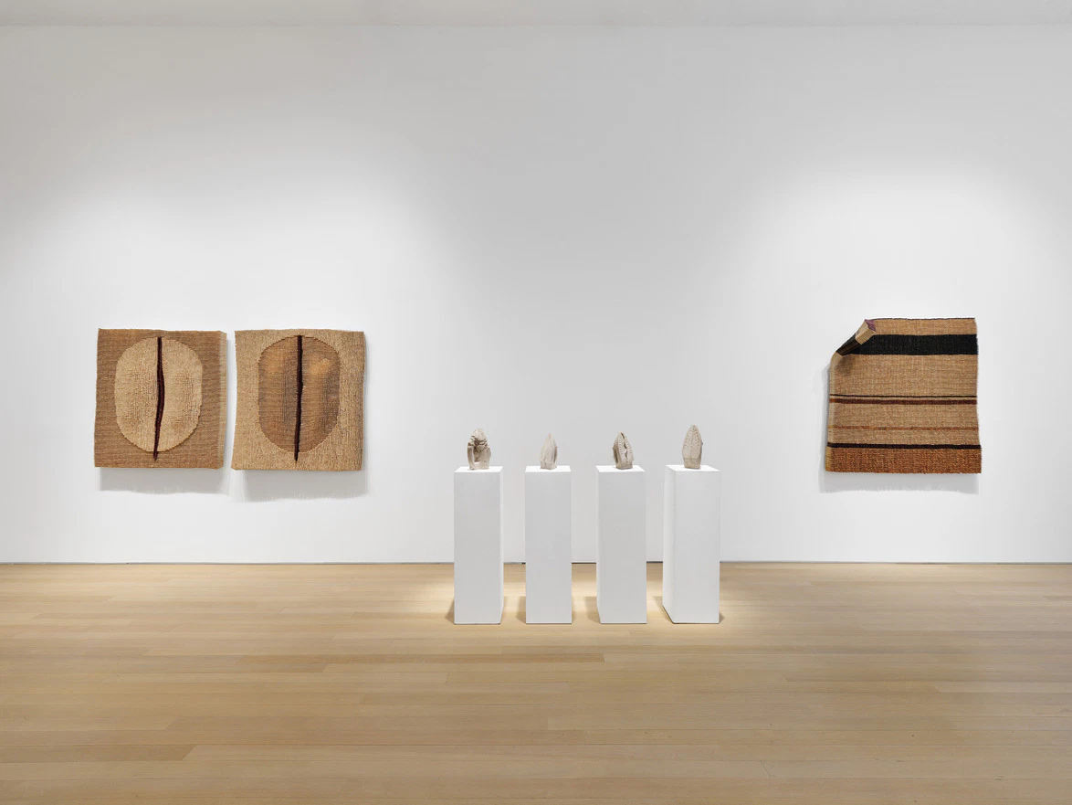 Art gallery interior with modern abstract woven artworks on walls and sculptures on white pedestals in a spacious room.