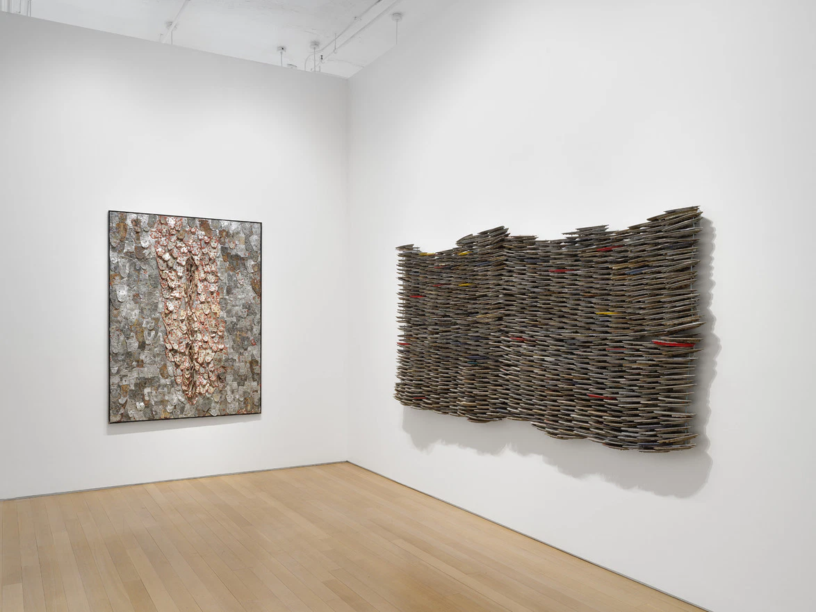 Contemporary art installation featuring a textured wall sculpture and a framed mixed media artwork in a modern gallery space.