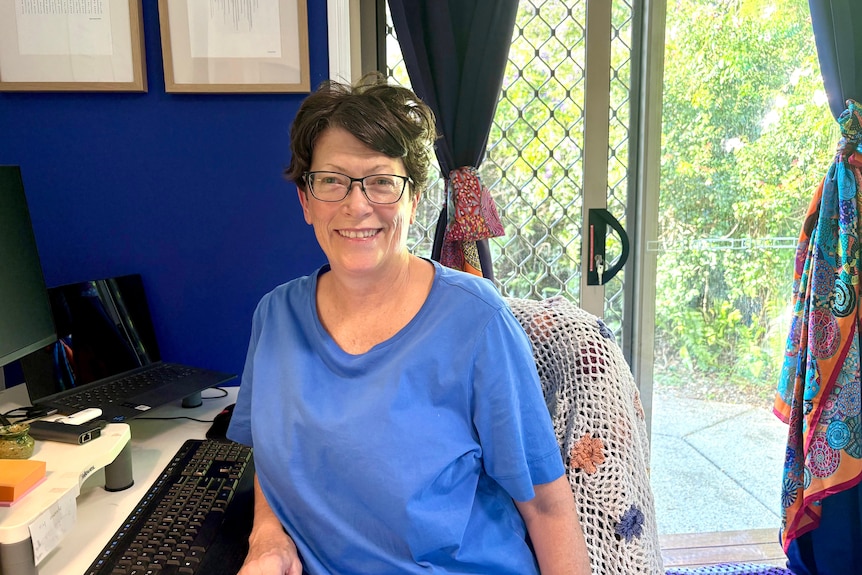 A woman wearing glasses sitting at a desk near a computer.