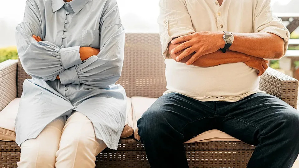 A married couple standing with arms crossed, looking angry and frustrated