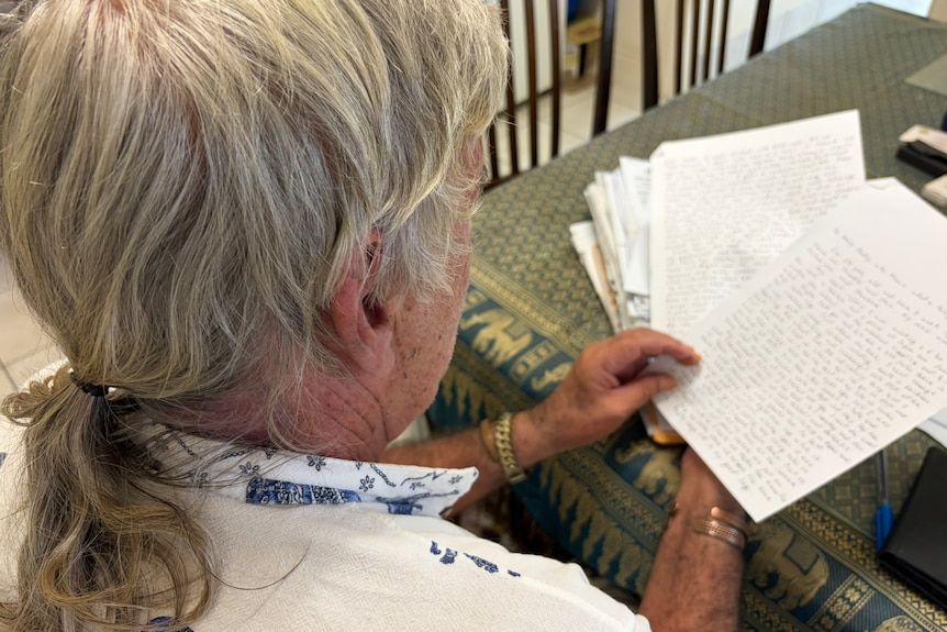 An older man sitting at his kitchen table with a large stack of papers.