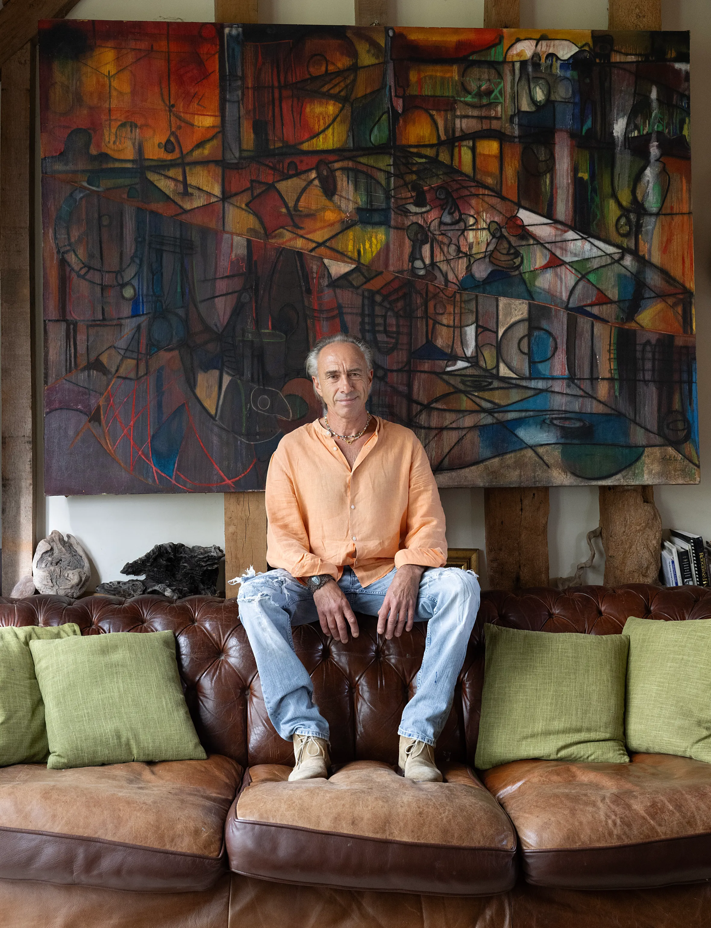 Clinton Pugh sitting on a brown leather couch in front of Sacha Jafri’s abstract painting "Eternal Journey".