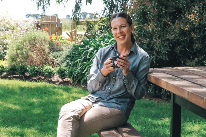 A woman sitting on a bench outside with a mug. 