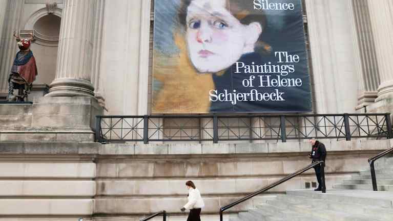 Two people on white steps below a large banner with a painting of a woman's face and the words: Silence: The Paintings of Helene Schjerfbeck.