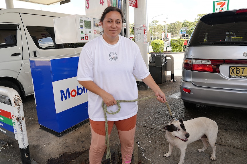 A woman holds a dog on a leash at a petrol station.