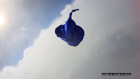 Blue fabric floating in a bright sky with clouds and sun.