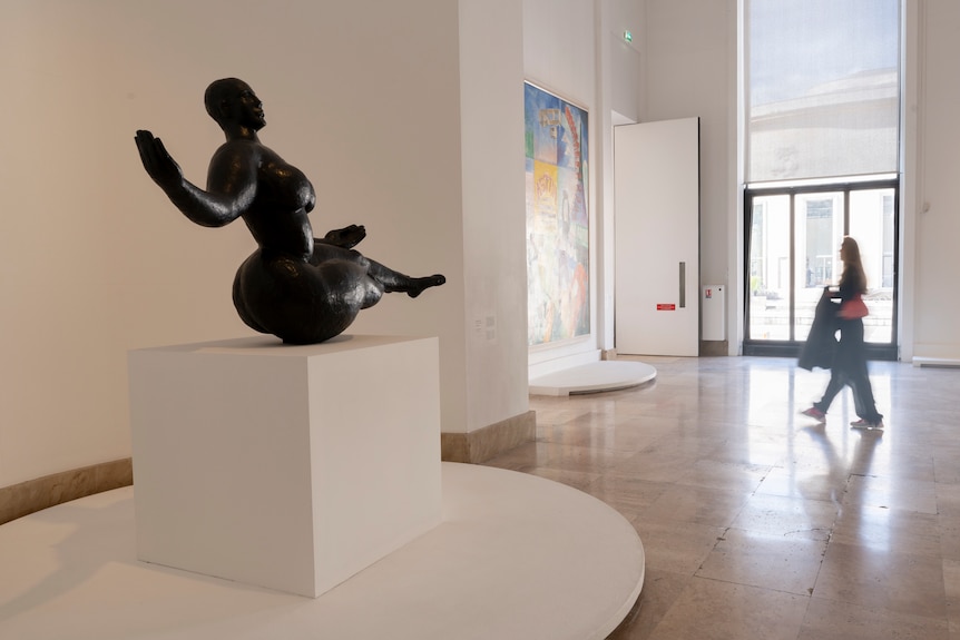 The inside of an art gallery, with a black sculpture of a naked woman on a plinth.