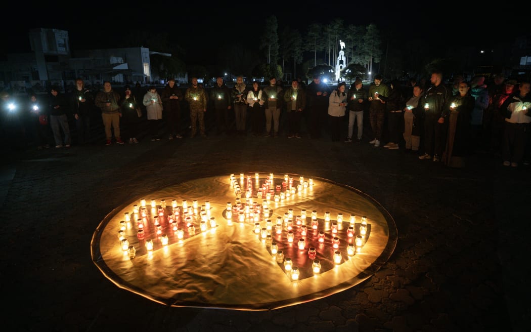 People hold candles during a commemoration ceremony marking the 40th anniversary of the explosion at the Chernobyl nuclear power plant, the worst civilian nuclear disaster in history, in front of a memorial for Chernobyl victims in the town of Slavutych on April 25, 2026, amid the Russian invasion of Ukraine. (Photo by Genya SAVILOV / AFP)