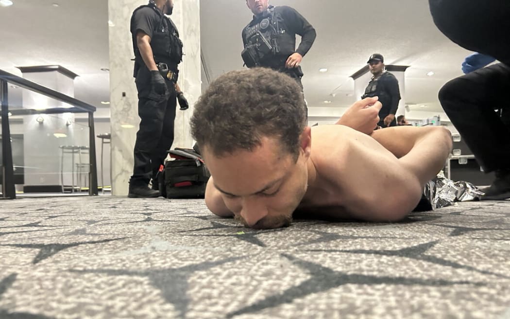 This image released by US President Donald Trump via his Truth Social account (@realDonaldTrump) shows a person he claims to be the alleged suspect in the shooting incident at the White House Correspondents’ Dinner on the ground after being apprehended on April 25, 2026. US Secret Service agents bundled Donald Trump from the stage as shots rang out Saturday evening at a media gala, in what the president later described as an attack by a