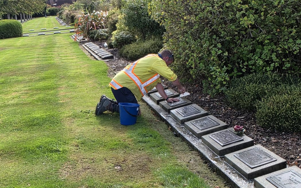 A volunteer cleans the gravestones of people who served New Zealand.