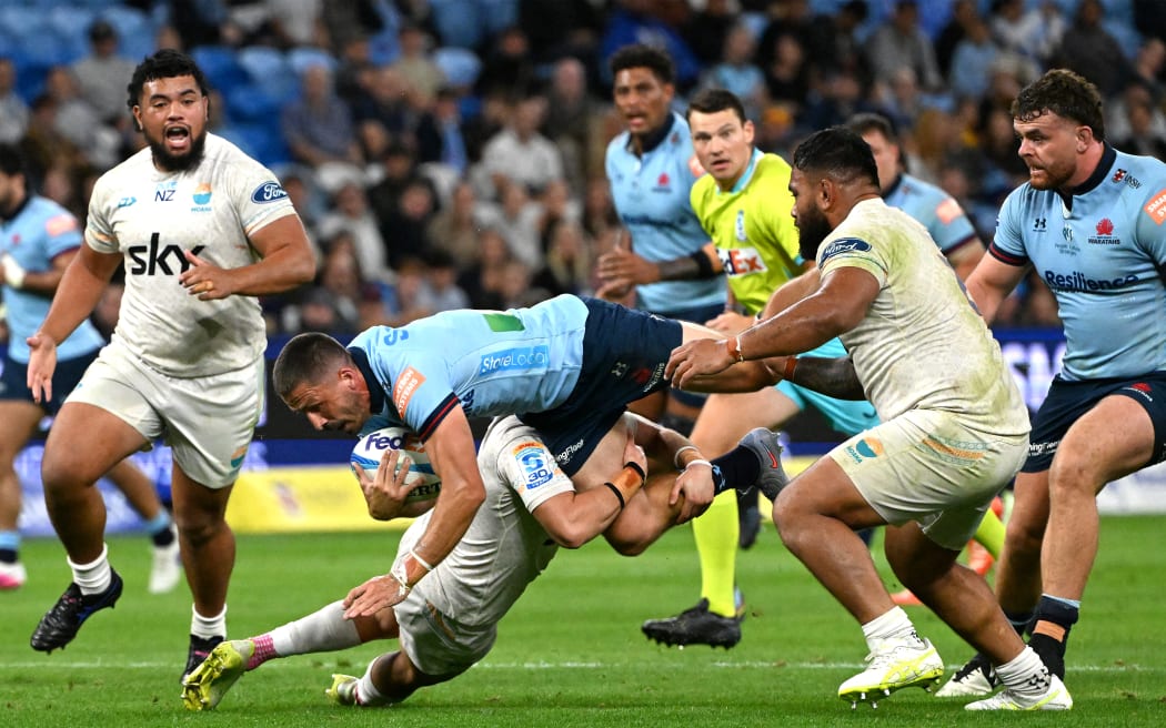 Waratahs' Jake Gordon (C) is tackled by Moana’s Patrick Pellegrini (L) during the super rugby match between NSW Waratahs and Moana Pasifika at Allianz Stadium in Sydney on April 17, 2026. (Photo by Saeed KHAN / AFP) / -- IMAGE RESTRICTED TO EDITORIAL USE - STRICTLY NO COMMERCIAL USE --