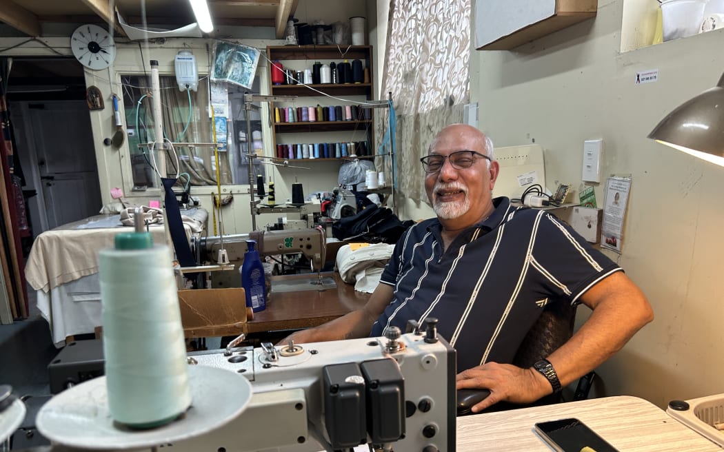 Picture depicts a 70-year-old man smiling behind a sewing machine.