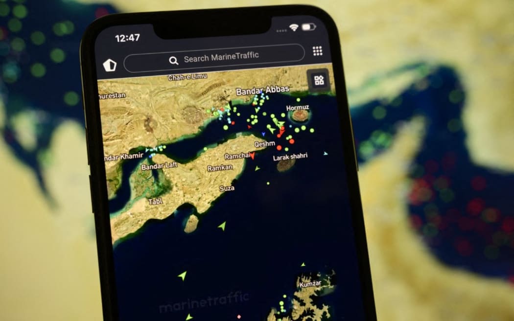 A smartphone displays the MarineTraffic app showing ship beacons near the Strait of Hormuz with a satellite view in the background, in Creteil, France, on April 8, 2026.