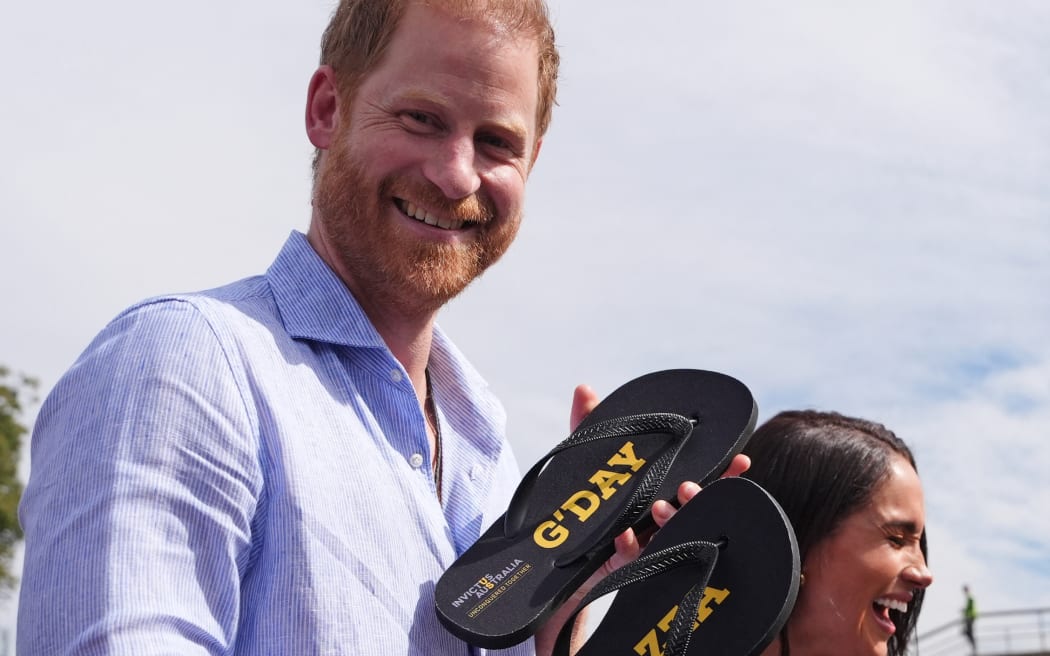 Britain's Prince Harry, Duke of Sussex, and his wife Meghan, the Duchess of Sussex, react after they received flip-flops with the inscriptions "G'day Hazza" and "G'day Megs" from veteran Joel Vanderzwan and his family before taking part in a sailing event with members of Invictus Australia in Sydney Harbour on April 17, 2026. (Photo by Jonathan Brady / POOL / AFP)