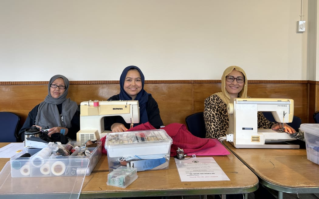 Picture depicts three women sitting behind sewing machines and smiling at the camera.