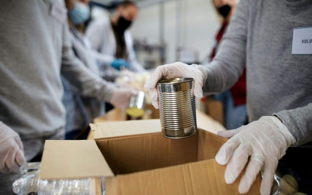 A person wearing gloves packs a can of food into a box for donation.