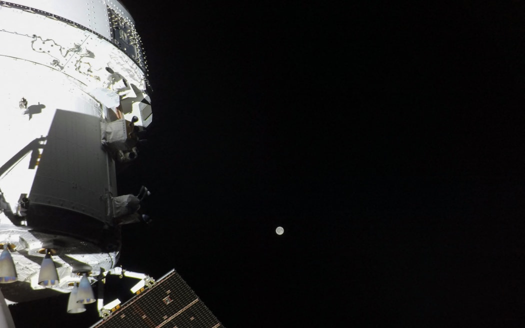 This handout picture provided by NASA shows the Orion spacecraft with the Moon in the distance, as captured by a camera on the tip of one of its solar array wings, on April 3, 2026. As Artemis II astronauts forged ahead on their lunar mission, NASA released initial images taken from the Orion spacecraft, including a full portrait of Earth featuring its deep blue oceans and billowing clouds. After a flurry of high-stakes activity including a dramatic blast-off and an engine firing that catapulted them on their historic trajectory to circle the Moon, the four astronauts aboard were able to catch their breath, even as they continued to perform a variety of equipment checks and tests. (Photo by NASA / AFP) / RESTRICTED TO EDITORIAL USE - MANDATORY CREDIT 