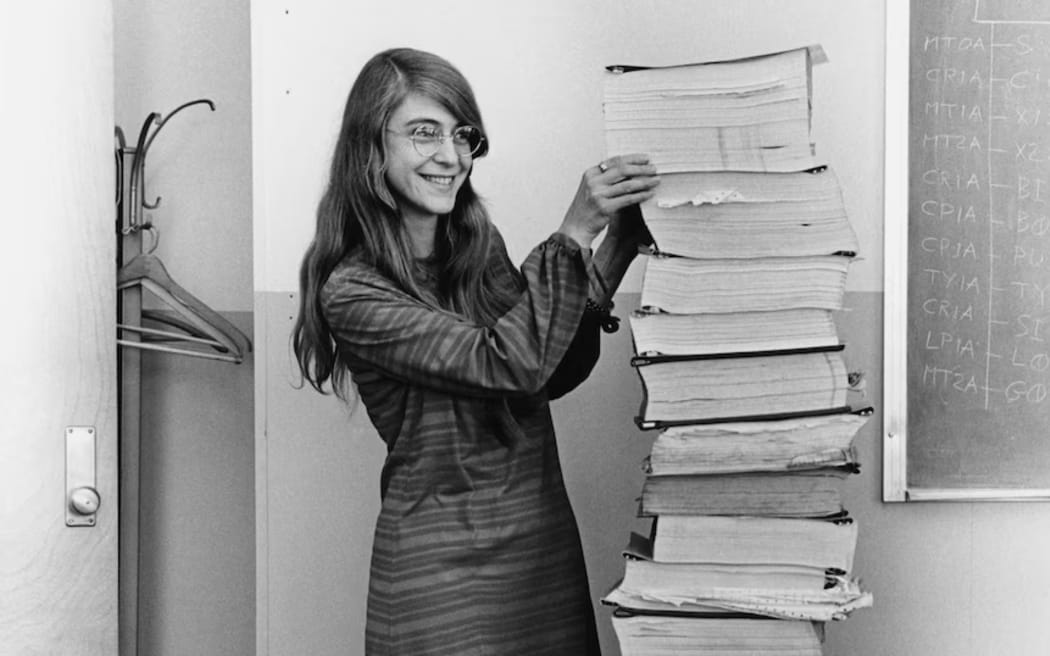 Margaret Hamilton stands next to a pile of flight software she led the development of as part of the Apollo Project. (Wikimedia Commons: Draper Laboratory, Margaret Hamilton, PDM)
