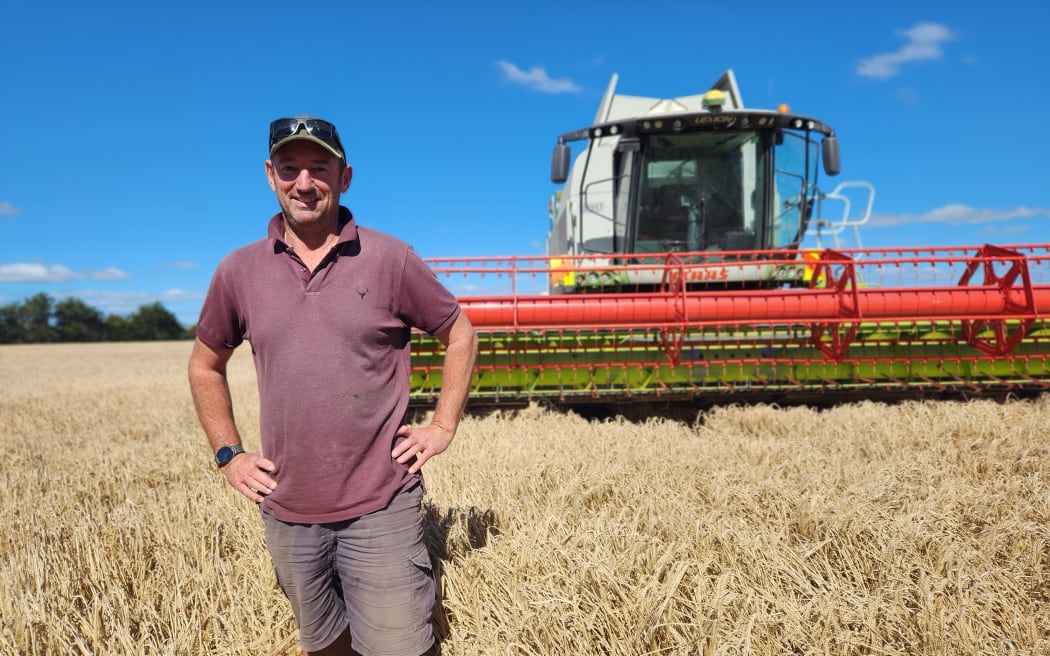 Mick Williams standing in a field of barley with his combine harvester in the background