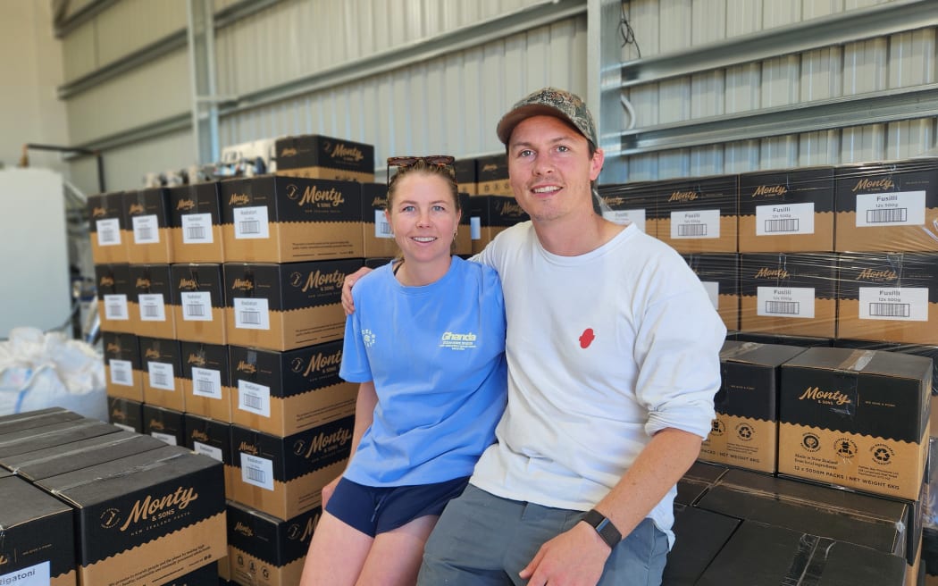 Jess and Monty Petrie sitting among boxes of their pasta