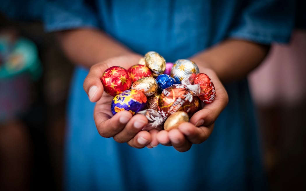 A person with cupped hands full of foil-wrapped Easter eggs.