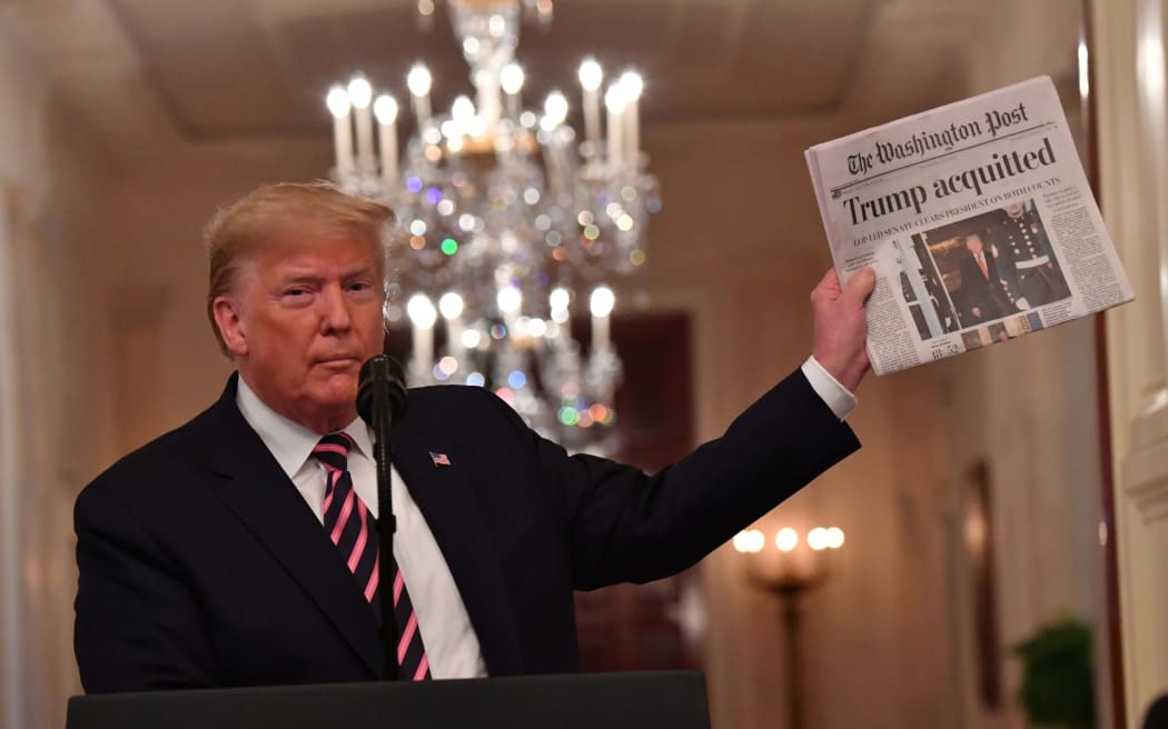 US President Donald Trump holds up a newspaper that displays a headline 
