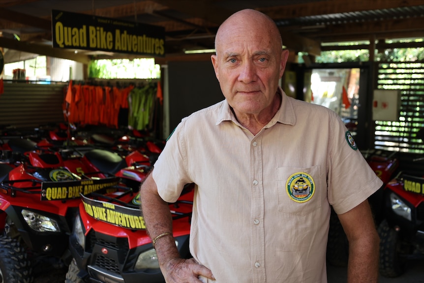 A bald man wearing a tan-coloured button up shirt with his hand on his hip