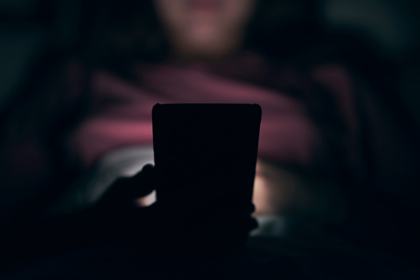 A hand holds a mobile phone in a dark room.