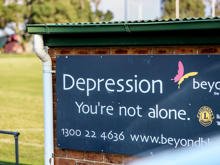 A sign affixed to the back of a brick structure next to a football oval that reads 'Depression, you're not alone'
